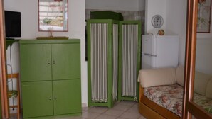 A small room with a green wardrobe, a white refrigerator, a beige sofa, and a wall clock.