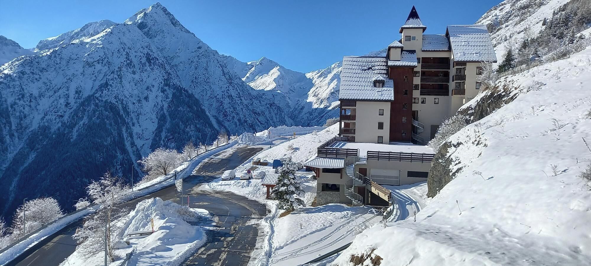 A snow-covered mountain resort with a multi-story building featuring balconies and a ski lift.