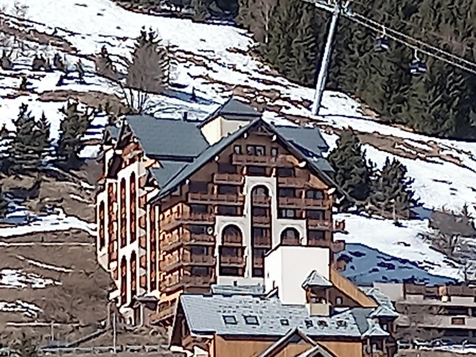 Un grand bâtiment en bois à plusieurs étages, doté d’une tour centrale imposante, entouré de collines et d’arbres recouverts de neige.