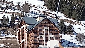 Un grand bâtiment en bois à plusieurs étages, doté d’une tour centrale imposante, entouré de collines et d’arbres recouverts de neige.