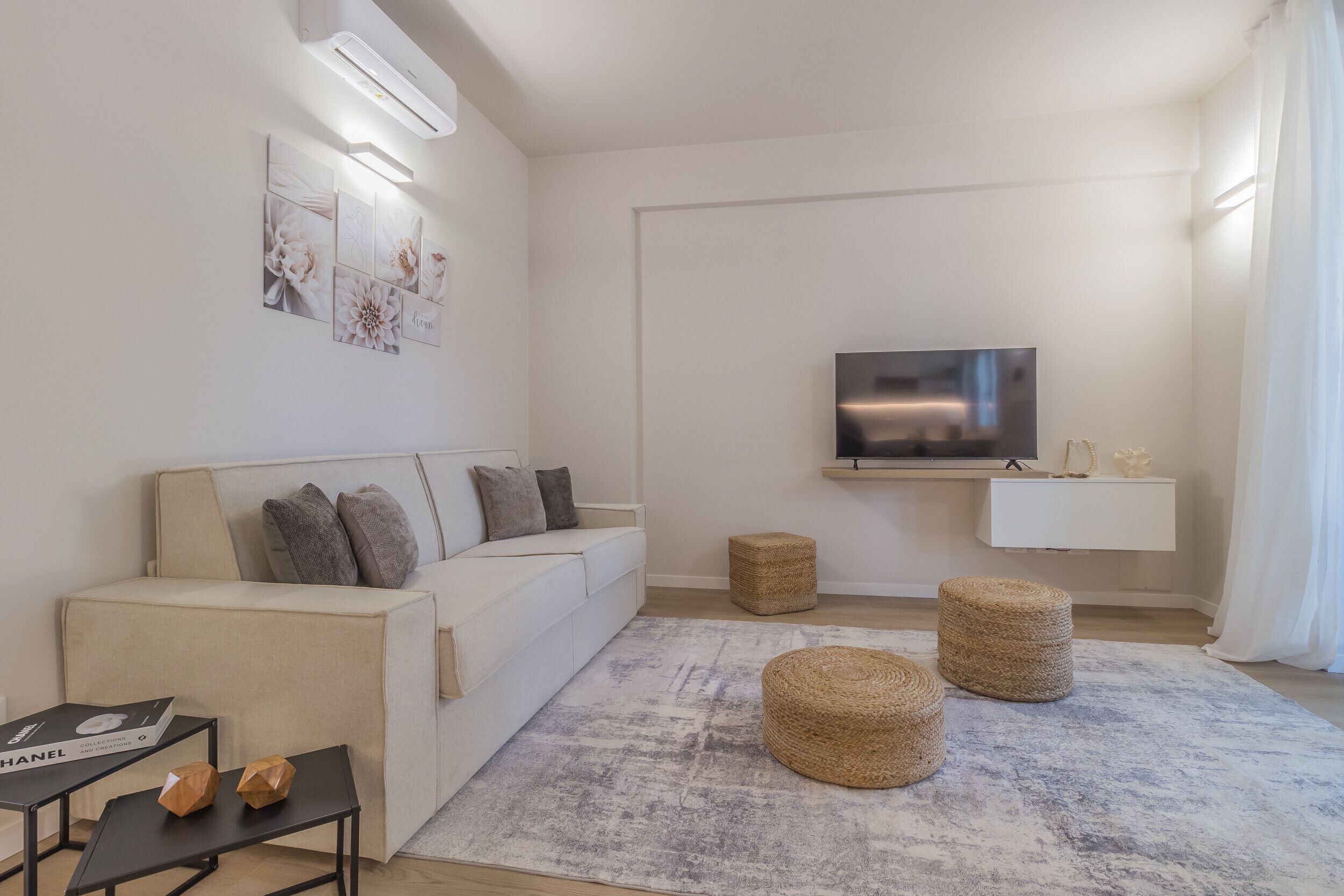 A modern living room with a sofa, a flat-screen TV, a coffee table, and two ottomans.