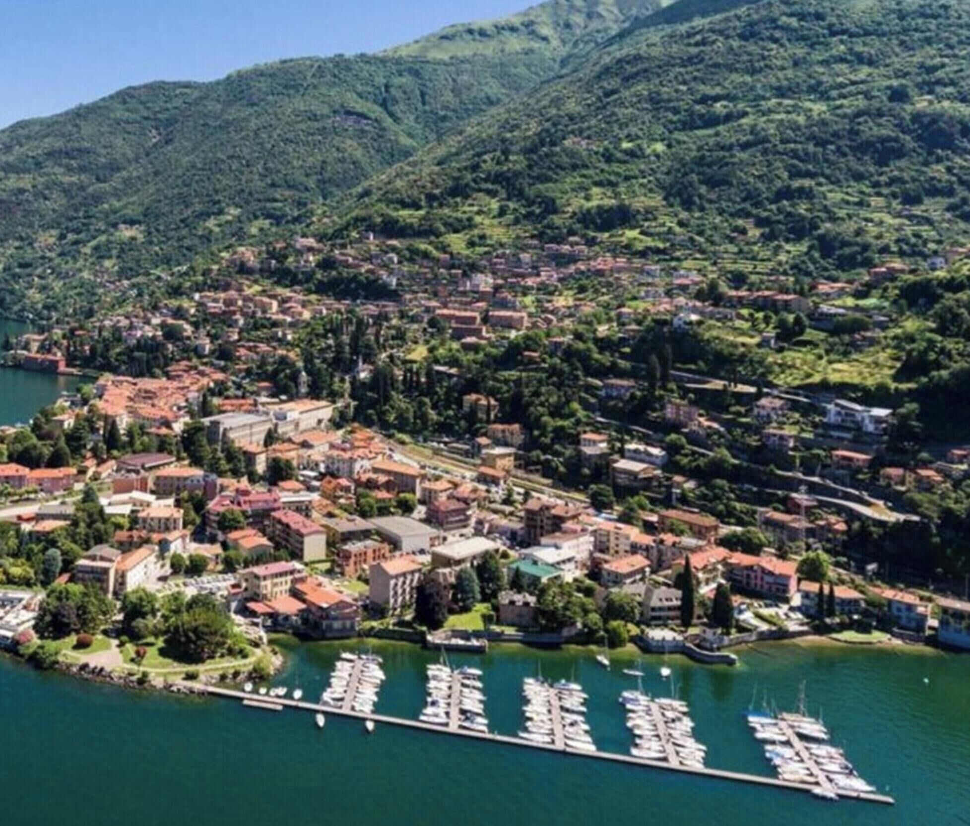 Vista aérea de un pueblo costero con edificios, un puerto deportivo y montañas al fondo.