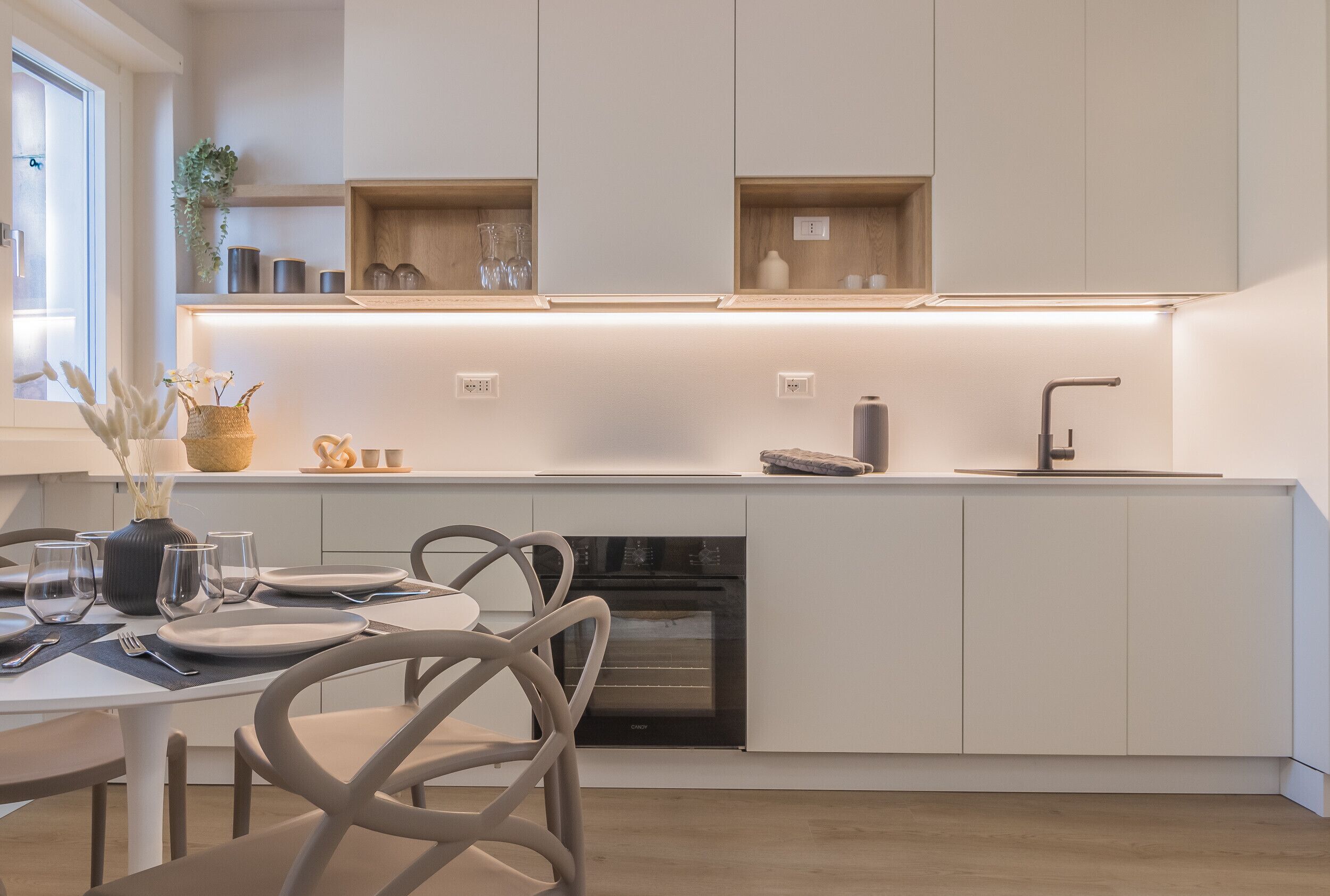 Una cocina moderna con armarios blancos, horno empotrado y comedor con mesa y sillas.