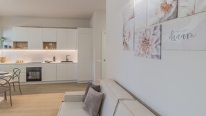 Ett modernt kök med vita skåp, en inbyggd ugn och en matplats med ett vitt bord och stolar.