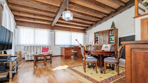 A wooden-floored living room with a sofa, a dining table, chairs, a bookshelf, and a television. - Triple Room with Mountain View, Shared Terrace and Wi-Fi (Telti)