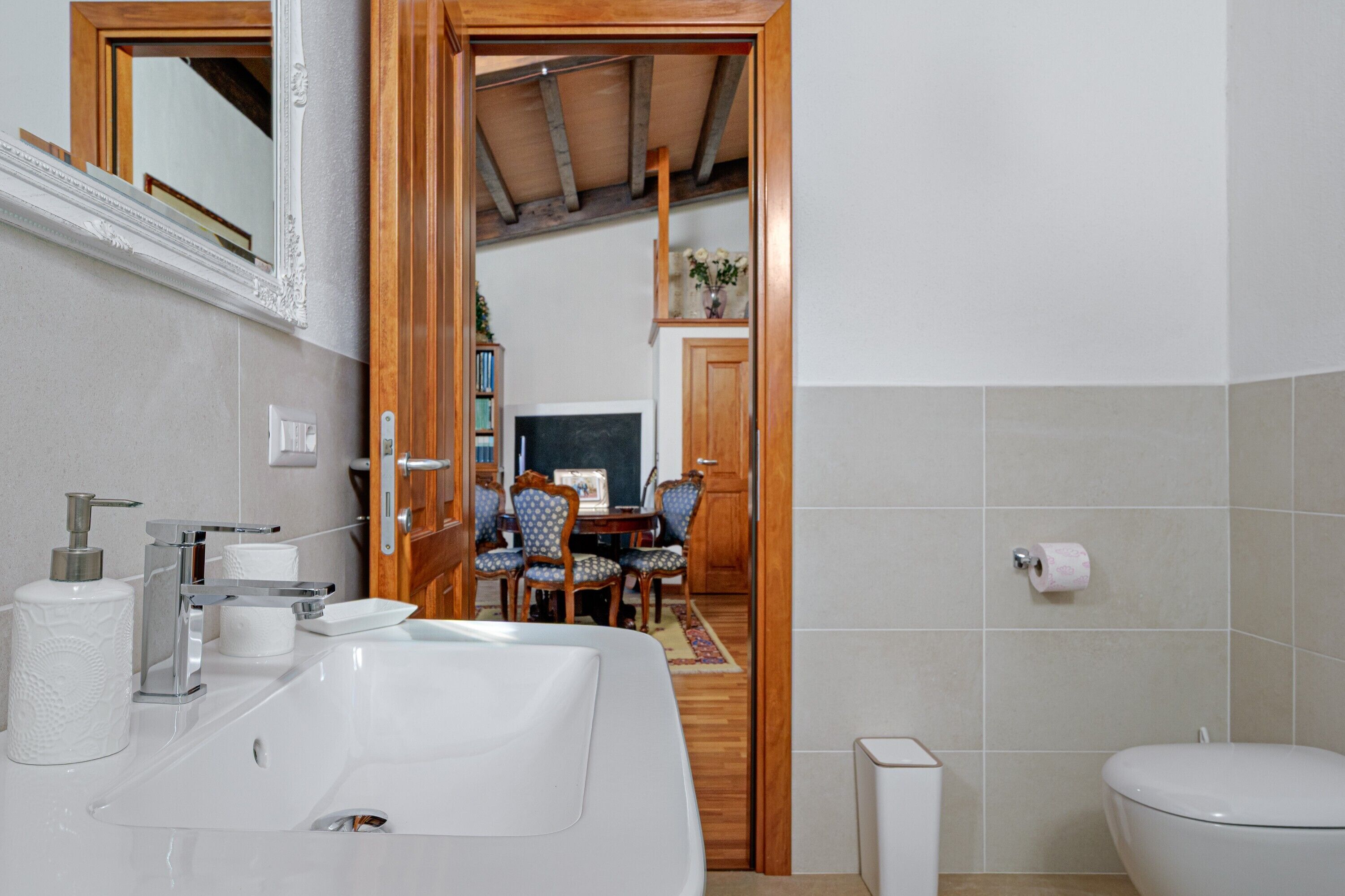A bathroom with a sink, toilet, and a wooden door leading to a dining area.