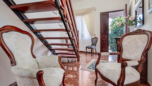 A staircase with wooden railings, two upholstered chairs with intricate designs, a patterned rug, and a door leading to an outdoor area with greenery. - Triple Room with Mountain View, Shared Terrace and Wi-Fi (Telti)