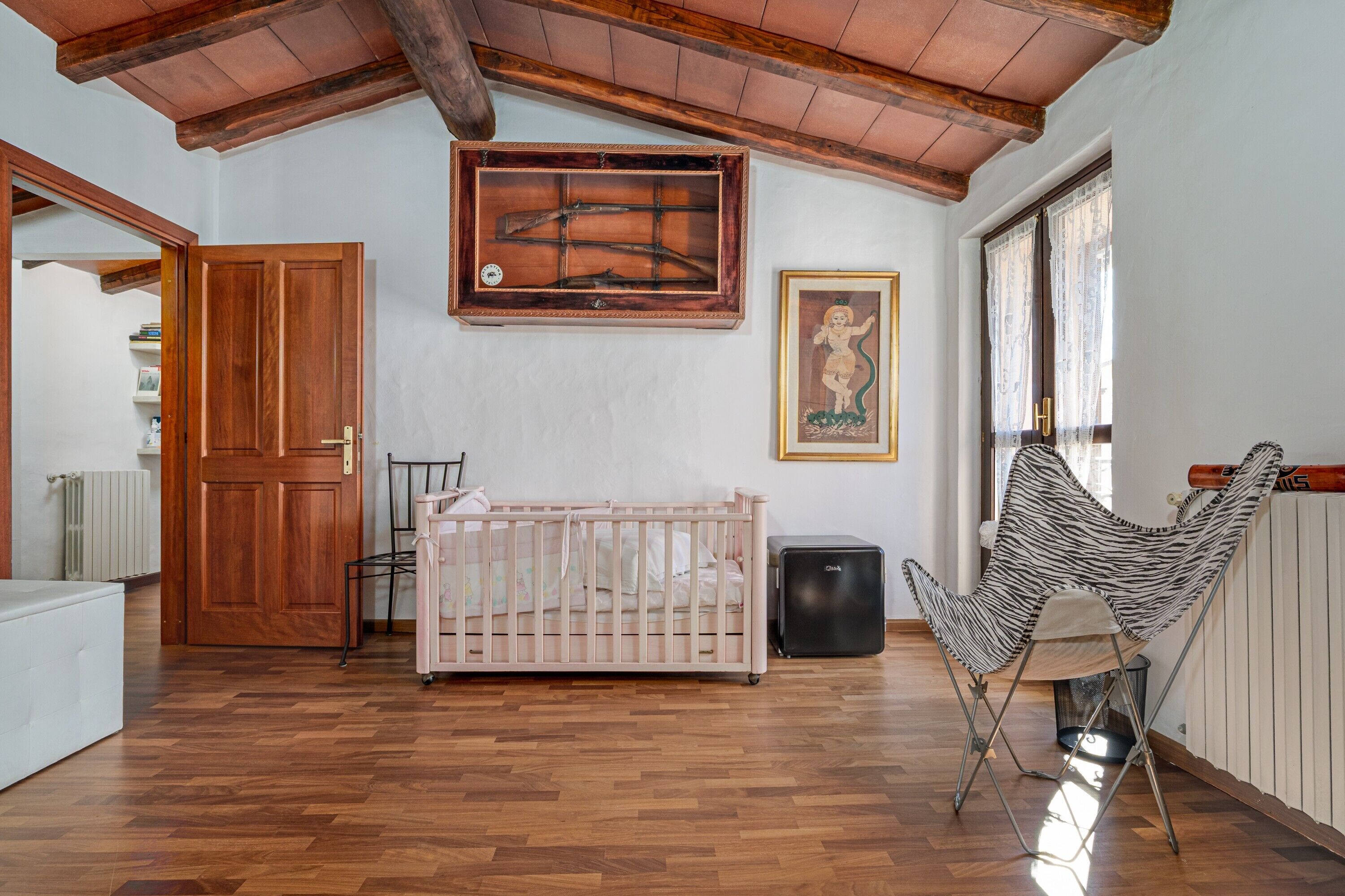 Una stanza con una culla, una poltrona a motivi zebrati, un termosifone e un soffitto in legno.