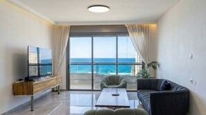 A living room with a TV, a sofa, a coffee table, and a view of the ocean. - Bright 3BR w/ Large Terrace & Sea View | Mamad (Bat Yam)
