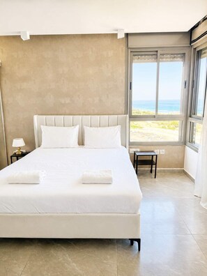 Ein Schlafzimmer mit einem großen Bett, einem Nachttisch, einer Bank und Blick auf den Strand.