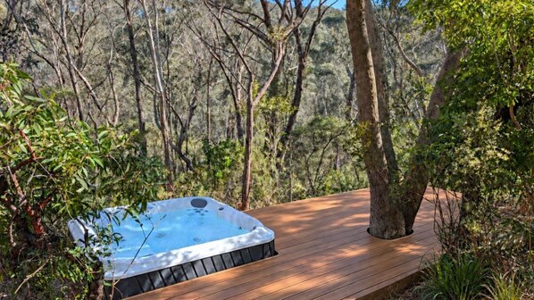 Ein Whirlpool auf einer Holzterrasse, umgeben von Bäumen.