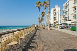 Une promenade en bois agrémentée de bancs, de palmiers et offrant une vue sur la plage et l’océan.