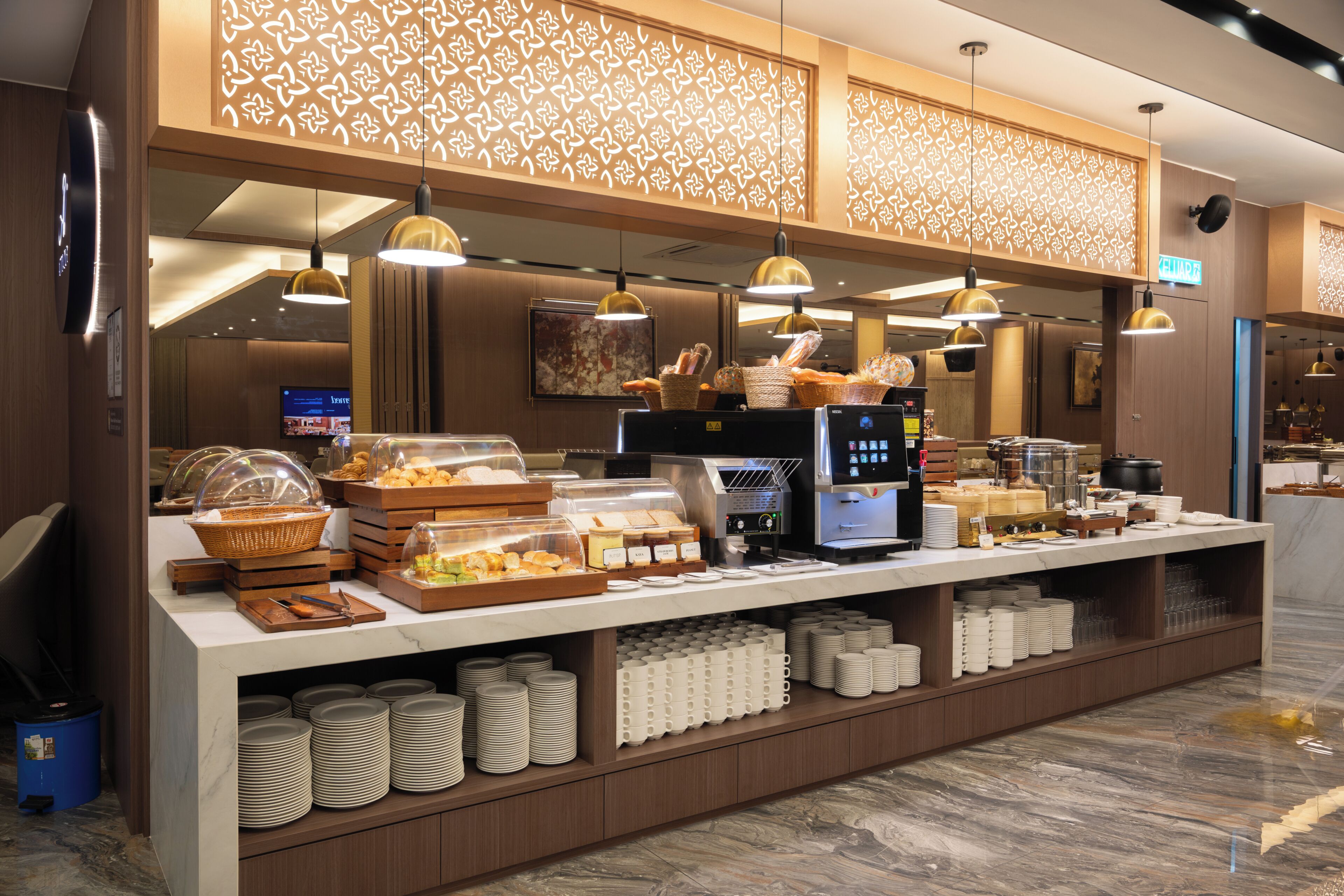 Disposição de buffet com diversos alimentos, uma máquina de café e um balcão com pilhas de pratos.