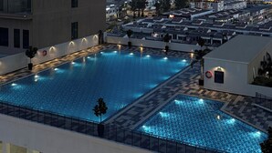 A large rectangular swimming pool with a tiled deck surrounding it, set within a modern building with multiple floors. - Asteria Melaka by Attic Suite (Malacca City)