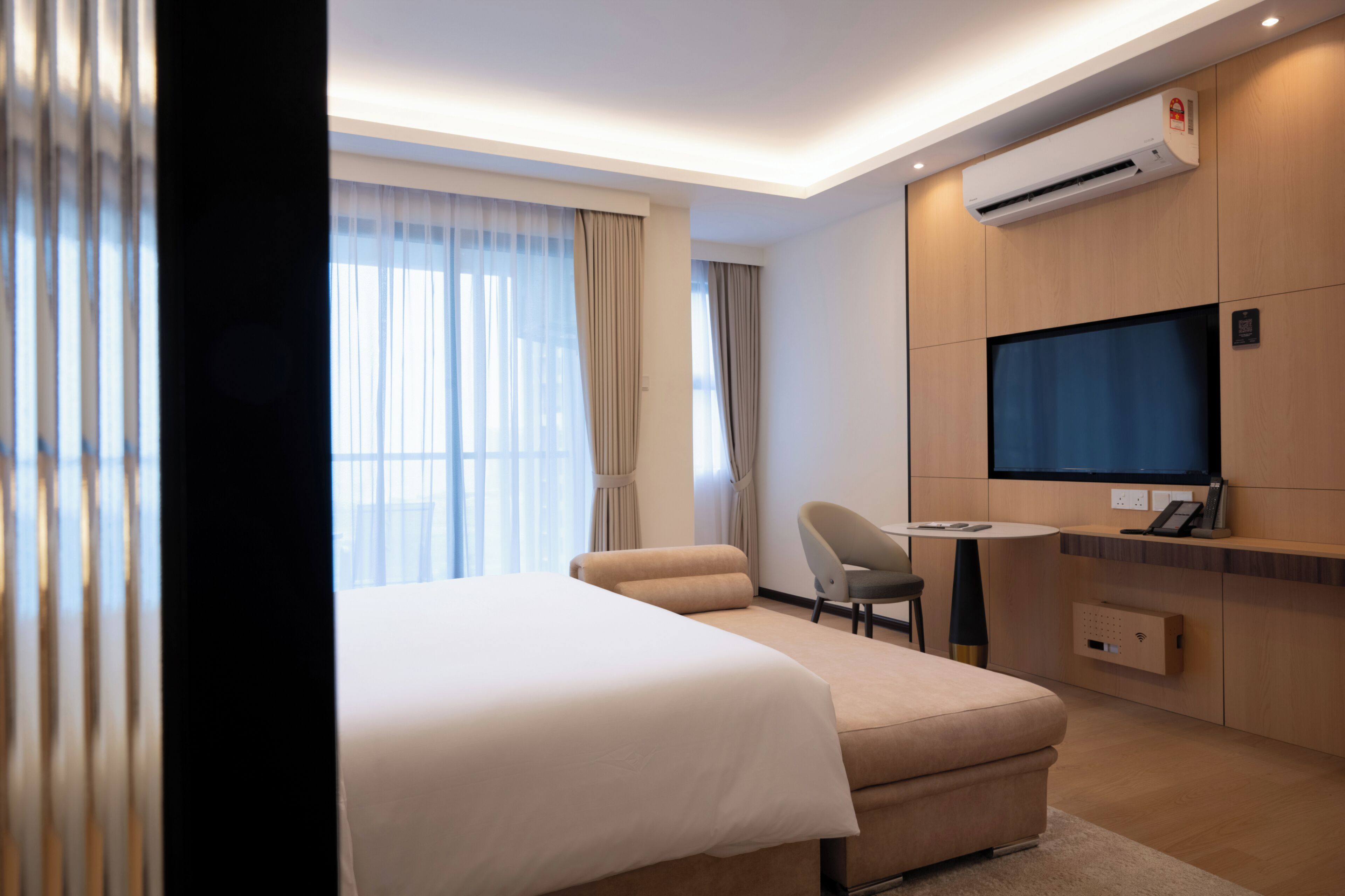 A hotel room with a bed, a desk, a chair, an air conditioning unit, and a television.
