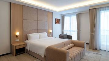 A modern hotel room with a large bed, a sofa, a nightstand, and a wall-mounted lamp.