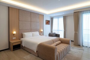 Una habitación de hotel moderna con una cama grande, un sofá, una mesita de noche y una lámpara de pared.
