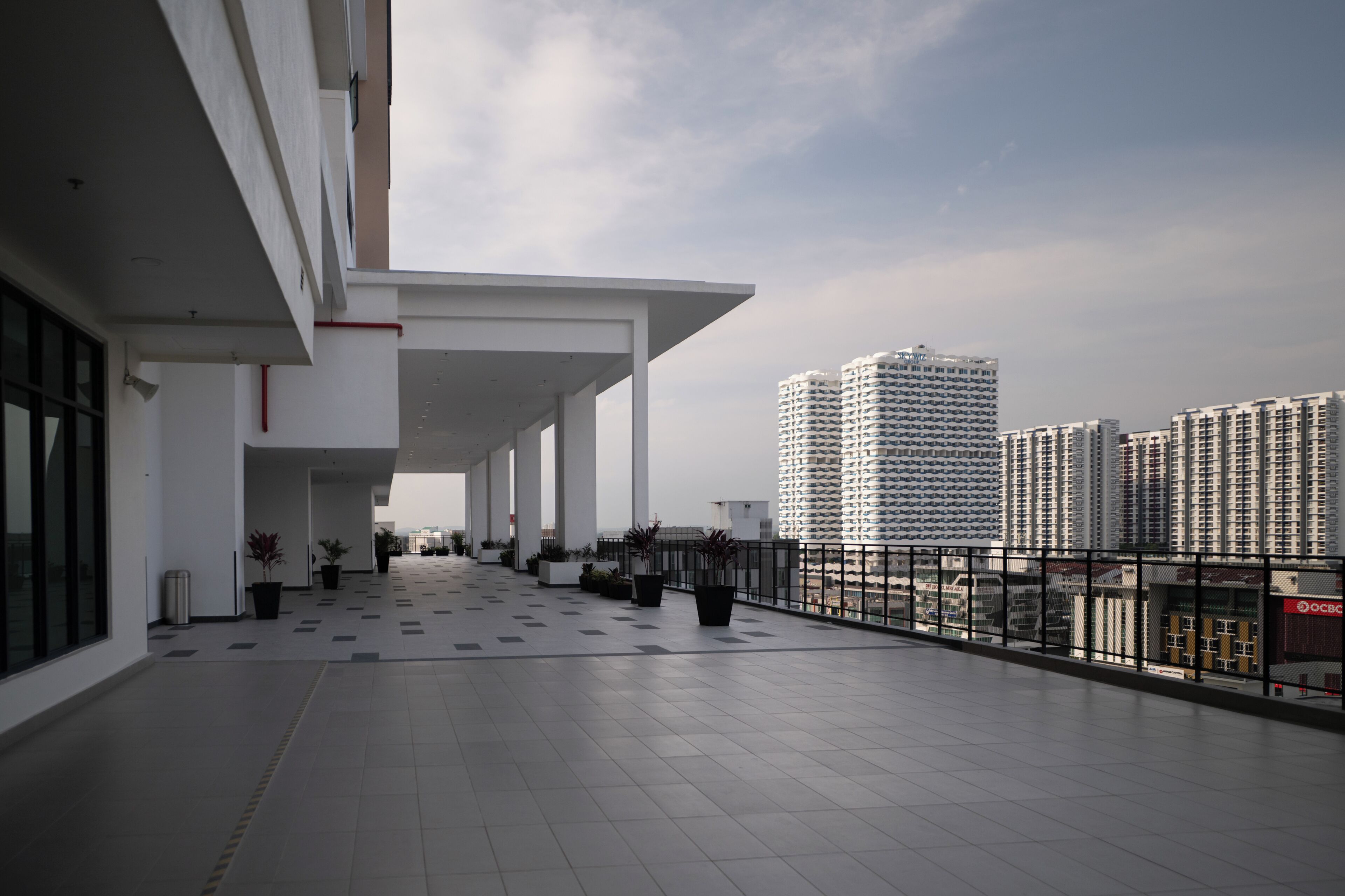 A spacious outdoor area with a tiled floor, potted plants, and a view of high-rise buildings in the background.