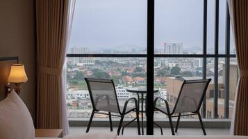 Quarto de hotel com uma janela grande, uma cama, duas cadeiras e uma mesa.