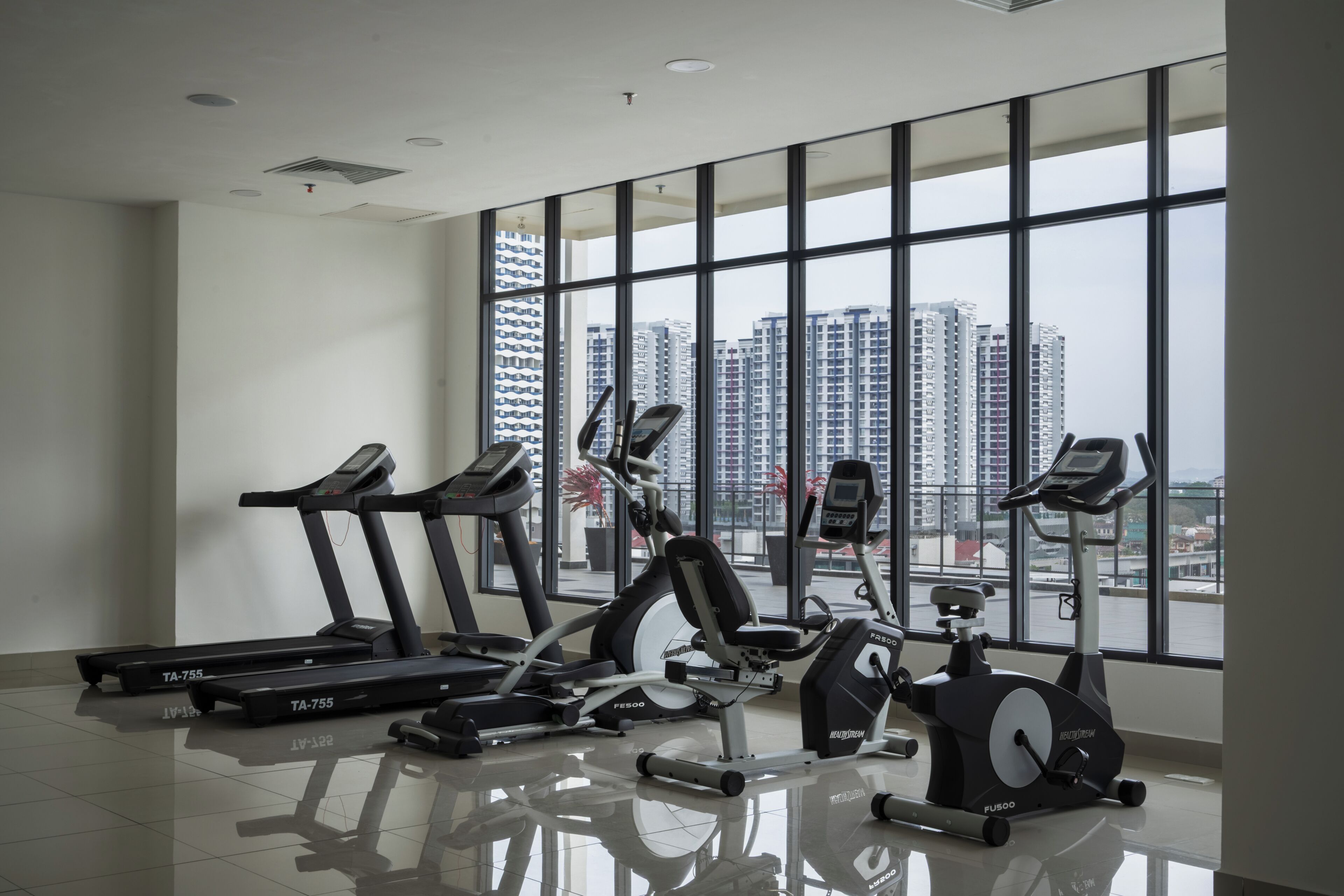 Un gimnasio con cintas de correr, elíptica y bicicleta estática, amplias ventanas con vista a la ciudad, y un diseño moderno y limpio.