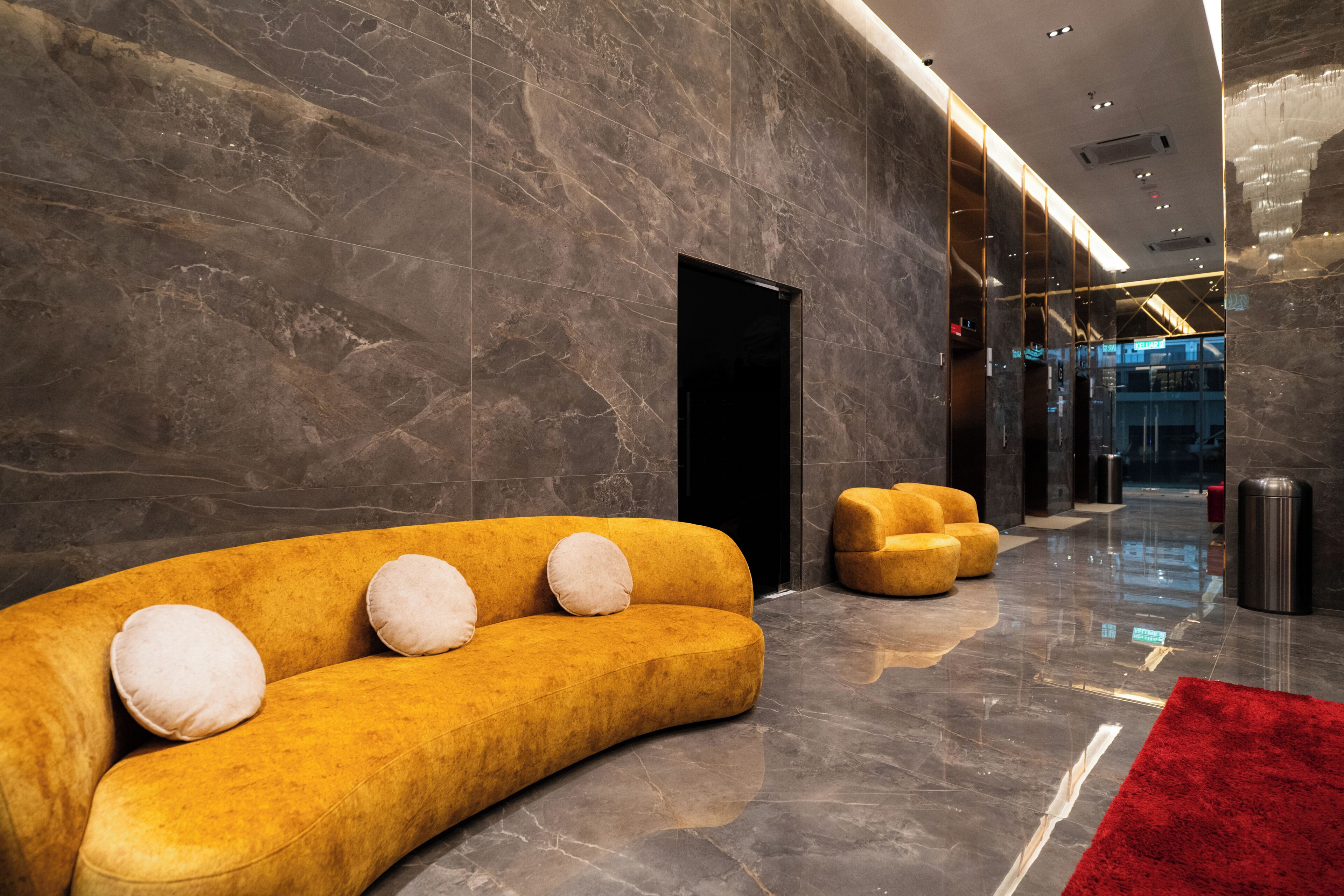 Un lobby moderno con un sofá amarillo curvado, una alfombra roja y paredes de mármol.
