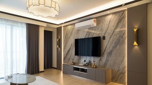 A modern living room with a flat-screen TV mounted on a marble wall, a round coffee table, and a sofa. - Asteria Melaka by Attic Suite (Malacca City)