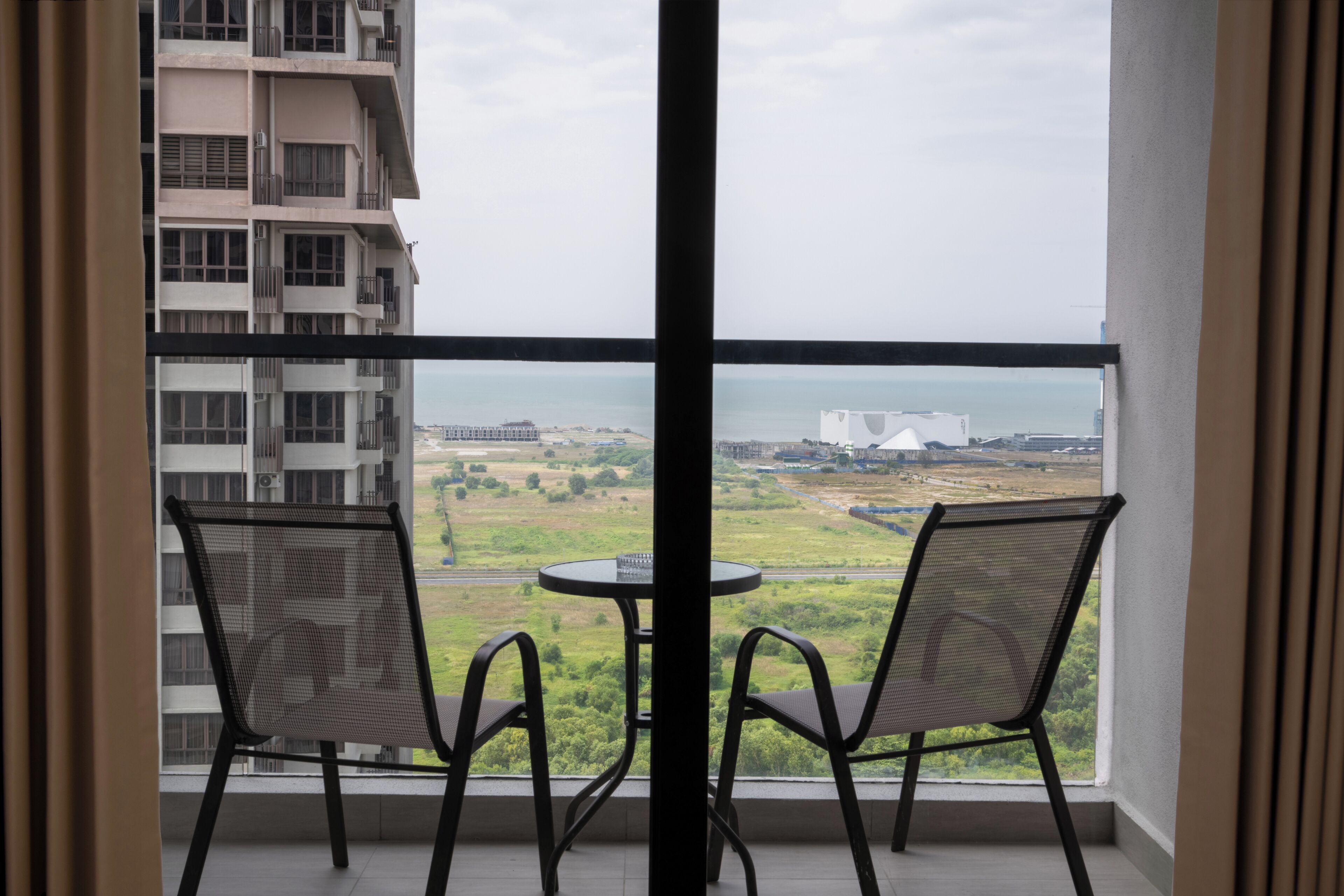 A balcony with two chairs and a table, overlooking a cityscape and a body of water.