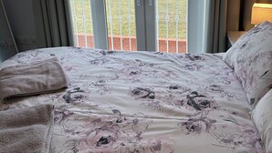 Ein Schlafzimmer mit Bett, Blick auf ein grünes Feld durch eine Glastür und einem Nachttisch mit Lampe.