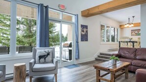 A spacious living area with a large window, a fireplace, and a cozy seating arrangement. - The Mountain House - Walk to the Village! (The Blue Mountains)