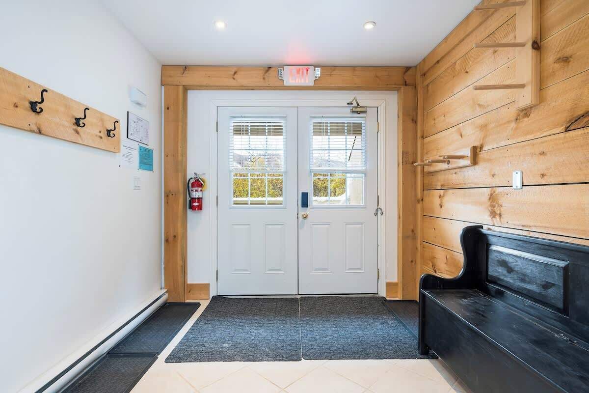 Un espace d’accueil avec un mur en bois, un banc noir, une porte à deux battants avec des fenêtres et un extincteur.