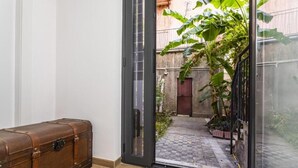 Una stanza con una porta vetrata scorrevole che dà su un cortile con pavimento a scacchi e piante in vaso.