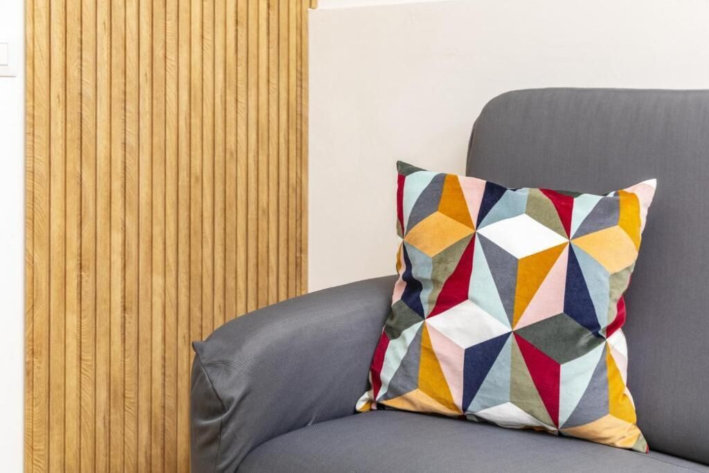 En grå sofa med en farverig geometrisk pude foran en væg af træpaneler.