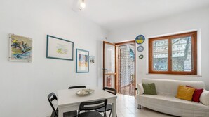 Un espace repas comprenant une table et des chaises, un canapé blanc avec des coussins et une porte donnant sur un espace extérieur.