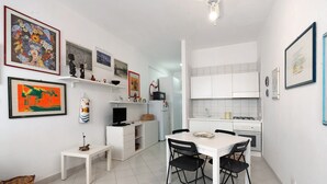 Une cuisine compacte avec des meubles blancs, une table à manger avec des chaises et diverses œuvres d’art accrochées aux murs.
