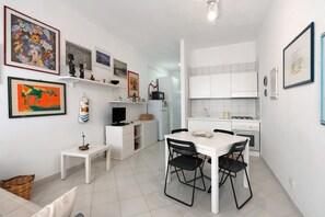 Een compacte keuken met witte kastjes, een eettafel met stoelen, en diverse kunstwerken aan de wanden.