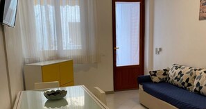 A small room with a glass table, a sofa, a yellow cabinet, and a door with a window. - Holiday Home 'Maltese' with Shared Terrace, Wi-Fi & Air Conditioning (San Vito Lo Capo)
