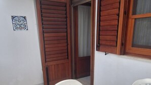 A room with wooden shutters, a white wall, and a small decorative tile. - Casa Concettina: Mountain View, Balcony & Air Conditioning (San Vito Lo Capo)