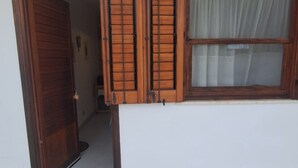 A wooden door, a window with a curtain, and a white wall. - Casa Concettina: Mountain View, Balcony & Air Conditioning (San Vito Lo Capo)