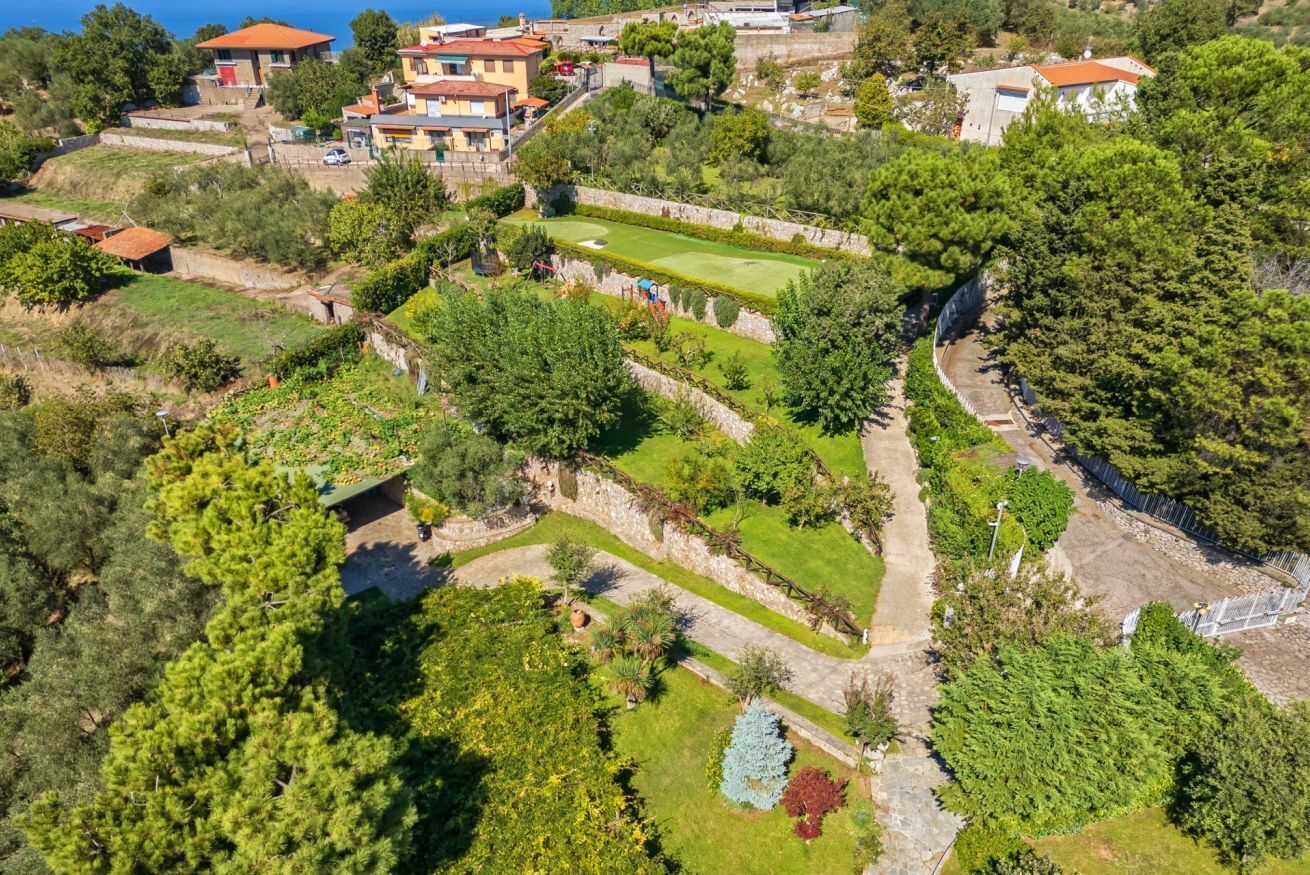 An aerial view of a hillside property with terraced gardens, stone walls, and residential buildings.