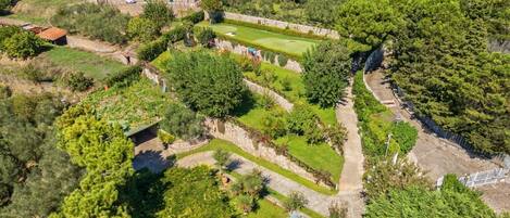 An aerial view of a hillside property with terraced gardens, stone walls, and residential buildings.