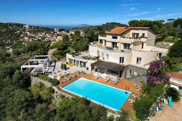 Uma villa grande e moderna com piscina, várias varandas e vista para o mar.
