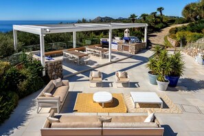 Um pátio externo com mobiliário, área de churrasco e vista para o oceano.