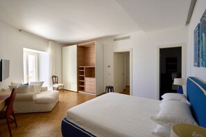 Quarto de hotel com cama, escrivaninha, cadeira, armário e um banquinho.