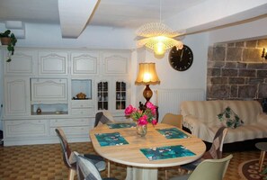 A dining area with a round table, chairs, a vase of flowers, a clock, and a stone wall.