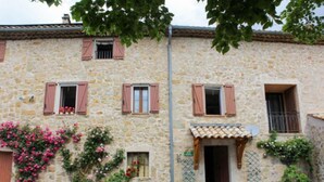 Un edificio in pietra con persiane rosa, un piccolo portone e un balcone.