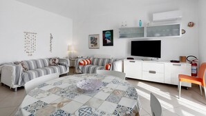A modern living room with a sofa, a dining table, a TV, and a white cabinet. - Holiday Home 'Berta' with Sea View, Private Terrace and Air Conditioning (San Vito Lo Capo)