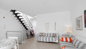A modern living room with a staircase, a sofa, a dining table, and a lamp. - Holiday Home 'Berta' with Sea View, Private Terrace and Air Conditioning (San Vito Lo Capo)