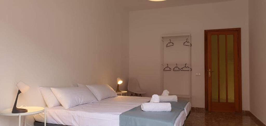 A bedroom with a bed, bedside tables, a lamp, a door, and a wall-mounted towel rack.
