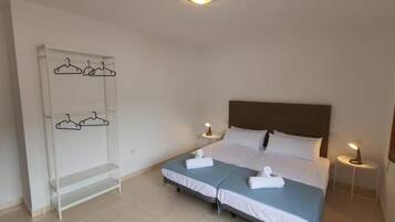 Habitación doble con dos camas, un armario con perchas, lámparas de noche y un espejo.