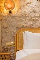 Una cama con ropa blanca, un cabecero de madera y una lámpara fijada a la pared.
